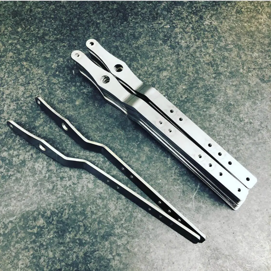 Batch of formed metal brackets with rows of drilled holes and larger tapped holes at one end
